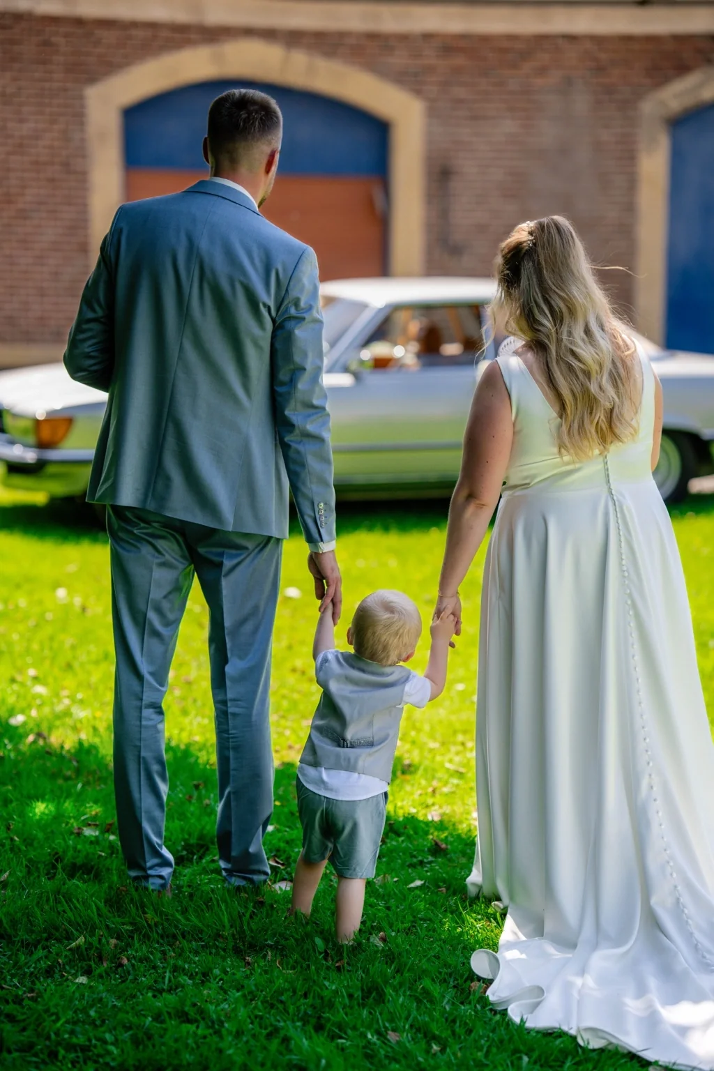 Brautpaar mit kleinem Kind Hand in Hand auf einer Wiese